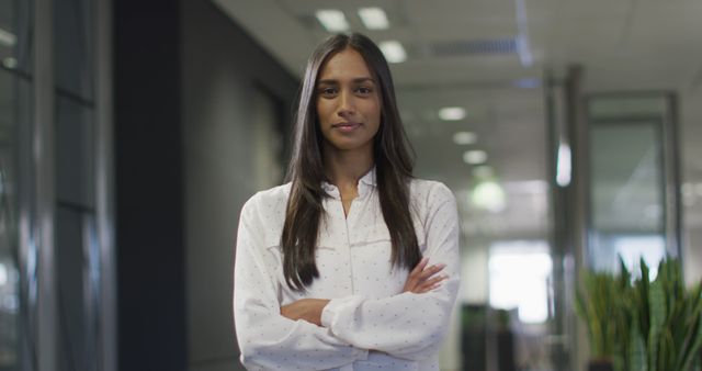 Businesswoman standing with arms crossed in an office setting, exuding confidence and professionalism. Ideal for use in business articles, corporate websites, promotional materials, career coaching, leadership promotions, and workplace culture illustrations.