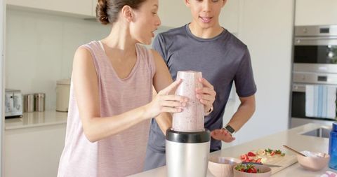 Young couple blending berry smoothie together on bright minimalist kitchen island morning