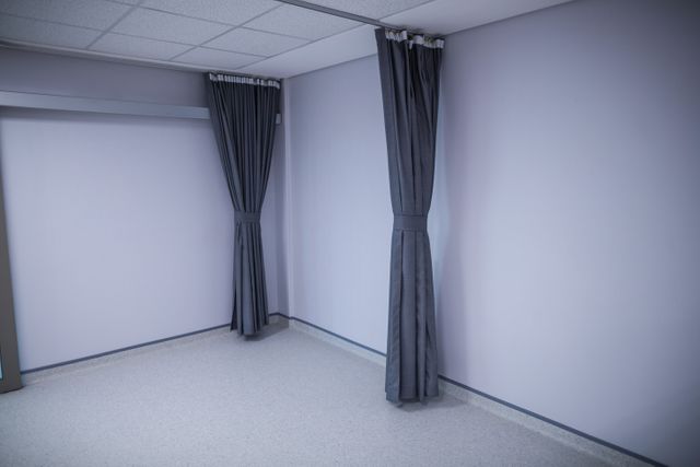 This image depicts an empty hospital room with privacy curtains. The clean and sterile environment is ideal for illustrating healthcare settings, medical facilities, and patient care. It can be used in healthcare brochures, hospital websites, and medical articles to convey a sense of cleanliness and professionalism.