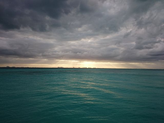 This image shows a striking contrast between stormy clouds and sunlight breaking through, casting light onto a calm ocean. Ideal for use in projects related to nature, weather phenomena, motivational backgrounds, and scenic beauty.