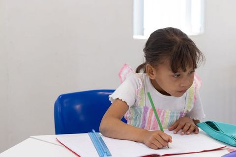 Concentrating schoolgirl writing in notebook at classroom desk with pencil and ruler