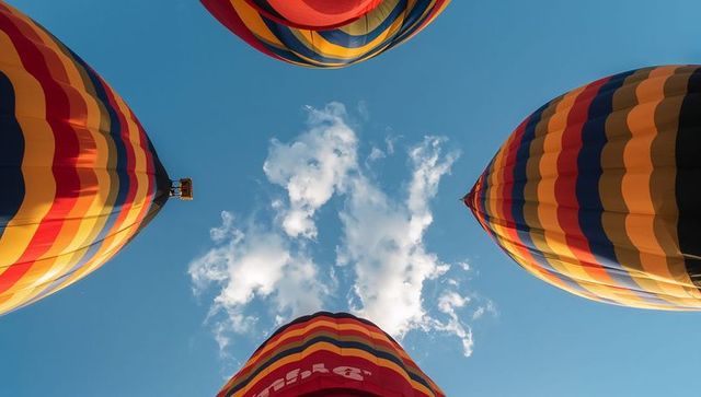Skyward striped hot air balloons framing upward launch over clear blue sky and clouds