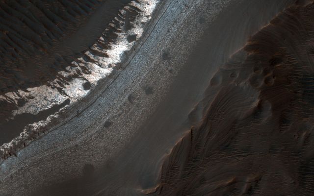 Aerial view of Holden Crater in Margaritifer Terra region on Mars, showcasing finely layered deposits caused by erosion and water flow. Spectacular outcrops visible along the breached crater rim. Useful for scientific research, educational materials, space exploration documentation, geological studies, and Mars mission planning.