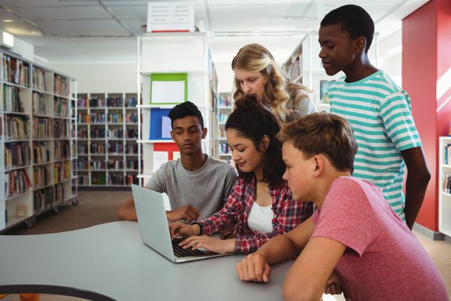 Group of students from diverse backgrounds collaborating on a laptop in a library. Ideal for educational content, teamwork and collaboration themes, technology in education, and academic research materials.