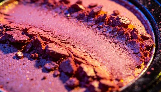 Crushed shimmering magenta eyeshadow pan macro with iridescent glitter texture