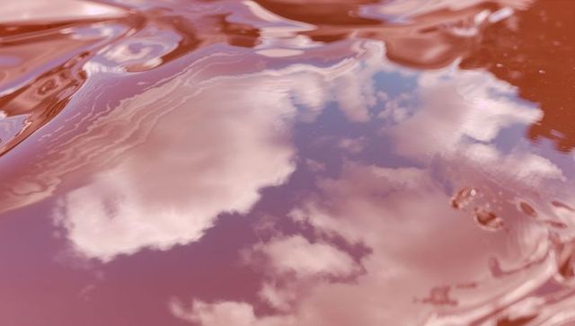 Pink liquid reflecting white cumulus clouds with rippling surface and shimmer