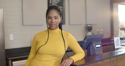 African american woman barista leaning on counter with pos and qr code in modern cafe