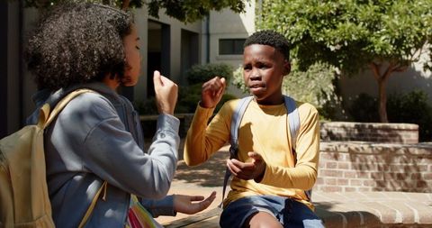 African-american teens playing hand game on school courtyard bench with backpacks