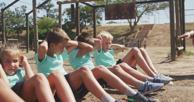 Determined caucasian boys and girls doing crunches in the sun at bootcamp training. Fitness, childhood, challenge and healthy lifestyle.