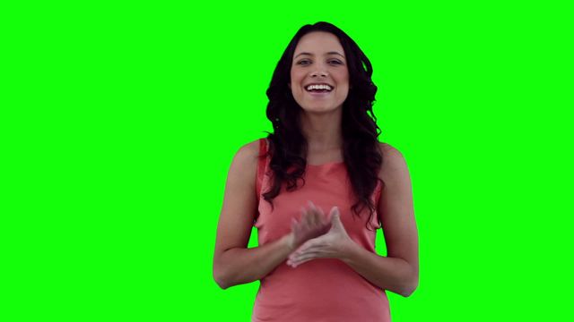 Woman standing in front of a vibrant green screen, smiling warmly as she gives a presentation. Could be used for video production, corporate training materials, or any content requiring a customizable background. The bright green screen allows for easy replacement with digital visuals.