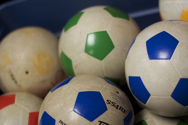 This image shows a close-up view of a pile of colorful soccer balls, showcasing various patterns and colors such as blue, green, and red patches. Suitable for use in sports equipment advertisements, recreational activity promotions, or as a visual representation of physical activities and team sports.