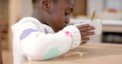 Child Eating Cereal from Bowl in Kitchen