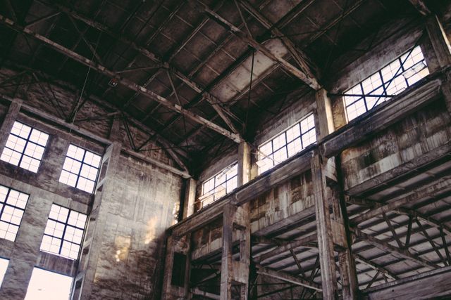 An abandoned industrial warehouse with large windows and metal framework showcasing rust and decay. Natural light streams through the broken and dirty windows, casting shadows on the distressed walls. The interior gives a sense of urban decay and history, making it ideal for themes of abandonment, industrial history, and vintage exploration.