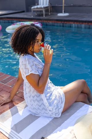 African american woman relaxing poolside sipping refreshing drink in white lace cover-up