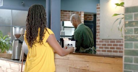 African american woman ordering takeaway coffee at rustic brick cafe counter