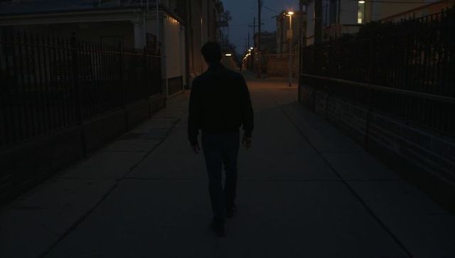 Walking silhouette down dim urban alley at dusk under glowing street lamps