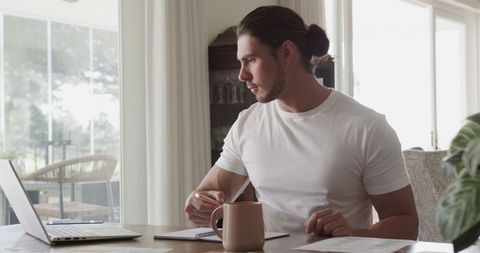 Focused Man Working Remotely on Laptop with Coffee at Home Office