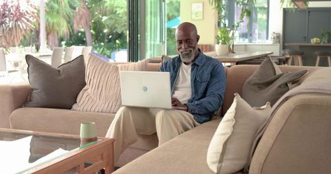 Senior african american man relaxing on sectional using laptop in bright modern living room