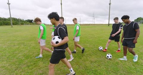 Diverse teenage boys at soccer practice with mesh bibs and soccer balls