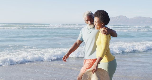 Senior couple walking along the beach with ocean waves in the background, showcasing togetherness and enjoying retirement. Ideal for promoting travel, senior living, happy lifestyles, romantic getaways, and outdoor activities.
