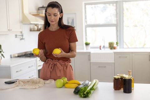 Woman in sunny farmhouse kitchen holding lemons preparing fresh groceries and healthy meals