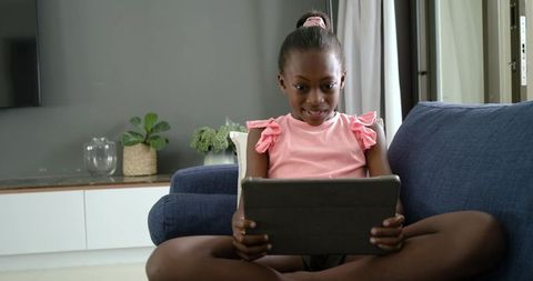African American Girl Using Tablet on Sofa Smiling and Learning at Home