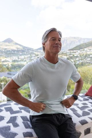 Mature man relaxing on terrace daybed with mountain landscape wearing mint t-shirt