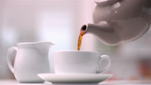 Teapot Pouring Tea into Cup in Cozy Indoor Setting