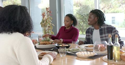 Multiethnic Friends Sharing Festive Dinner Around Wooden Table Passing Roast Bird