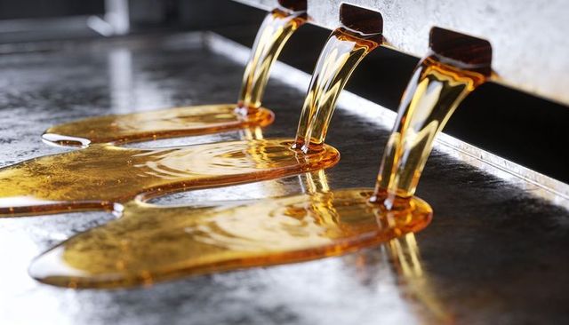Pouring golden maple syrup from triple stainless steel spouts onto hot griddle surface