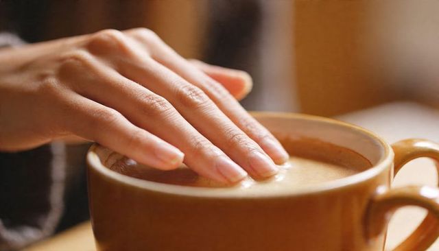 Pressing female hand creating foam ripple in ceramic coffee mug at cozy minimalist cafe