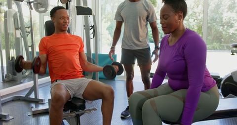 Couple gym training with personal trainer supervising