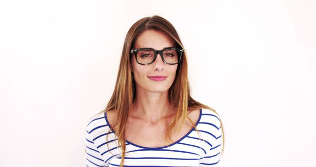 Young woman with long brunette hair wearing glasses and a striped top, standing against white background. This can be used in fashion websites, eyewear promotions, lifestyle blogs, or advertisements hoping to showcase modern, independent individuals.