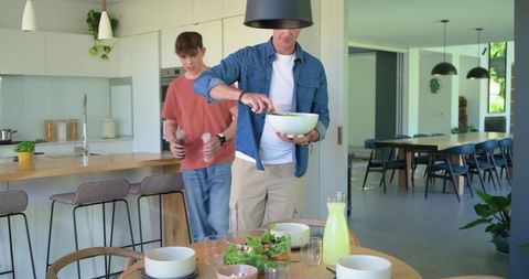 Father and teen son preparing fresh salad together in bright modern open-plan kitchen