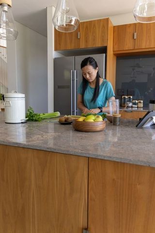 Asian woman chopping vegetables at marble kitchen island in warm modern kitchen
