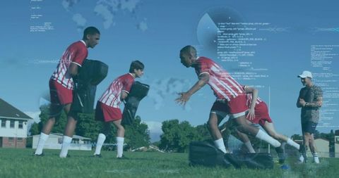 Youth team practicing tackle drill with blocking pads and coach on outdoor grass field