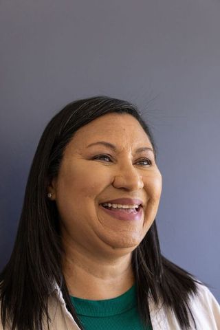 Smiling mature woman looking right wearing green top and light jacket, soft studio headshot