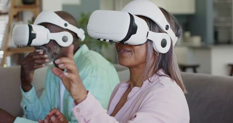 Senior couple enjoying virtual reality together with white VR headsets in living room