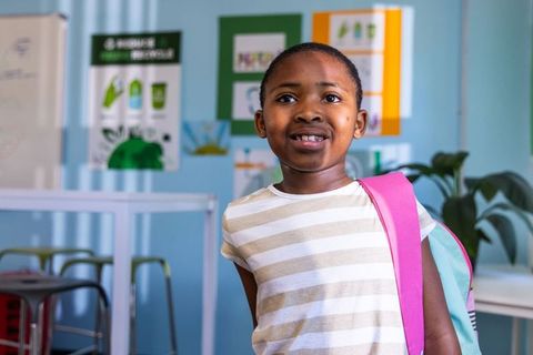 African american girl standing with pink backpack in classroom promoting recycling and learning