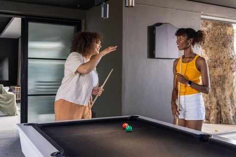 Diverse female friends playing pool and chatting in modern game room with black felt table
