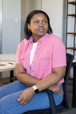 African american woman sitting modern office reviewing documents wearing pink shirt, jeans