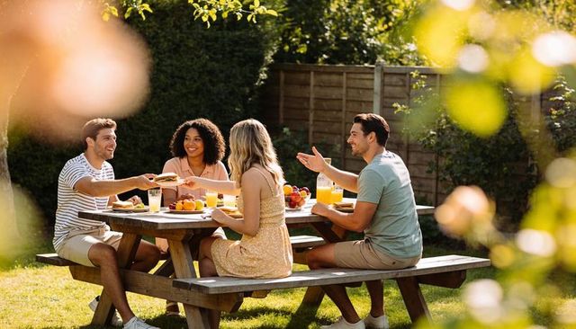 Friends enjoying summer backyard picnic at wooden table sharing food and drinks