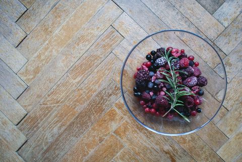 Frozen mixed berries with rosemary in glass bowl on herringbone wood floor