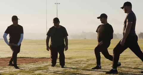 Senior Men Stretching and Lunging on Dewy Sports Field at Sunrise for Team Fitness