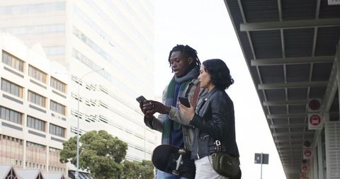 Diverse Young Adults Standing on City Transit Platform Checking Phones Holding Skateboard