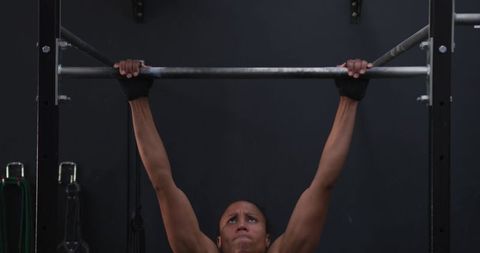 Strong african american woman performing pull-ups in gym
