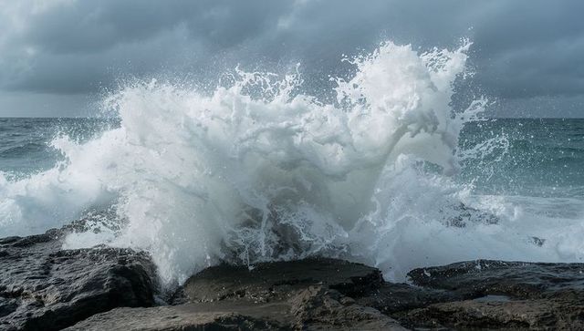 Roaring ocean wave crashing against dark rocky shoreline sending towering white spray