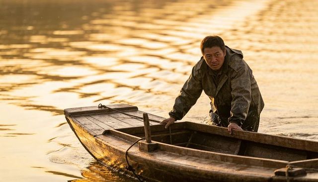 Wading fisherman guiding wooden boat through golden river reflections at sunset