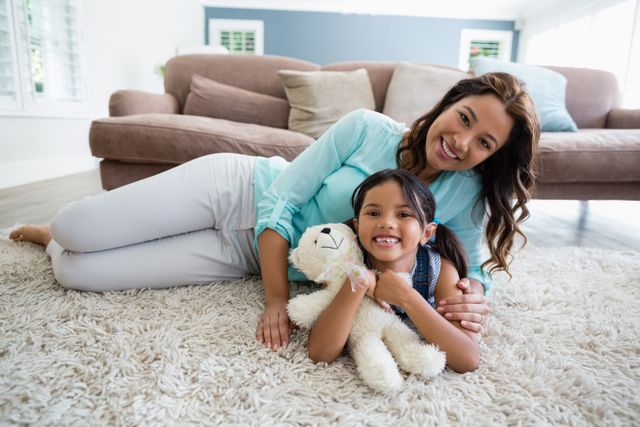 Mother and daughter lying on a rug in a cozy living room, smiling and bonding. Ideal for use in family-oriented advertisements, parenting blogs, and lifestyle articles focusing on home life and family relationships.