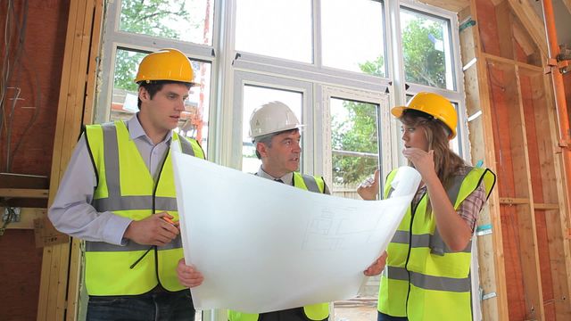 Group of professionals wearing safety gear discussing building plans at ongoing construction project. Useful for illustrating teamwork in construction, project management, planning phases in engineering, or safety compliance in infrastructure development.